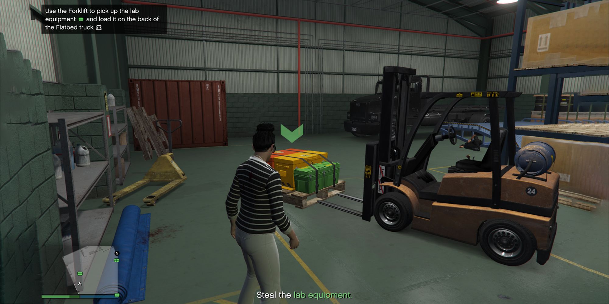 A imagem mostra um jogador do Grand Theft Auto Online parado em um armazém ao lado de uma empilhadeira amarela e um palete de equipamentos.  O palete tem uma seta verde apontando para baixo em cima dele.