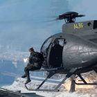 Image of Call of Duty player sitting on side of helicopter firing weapon at opponent standing on rooftop