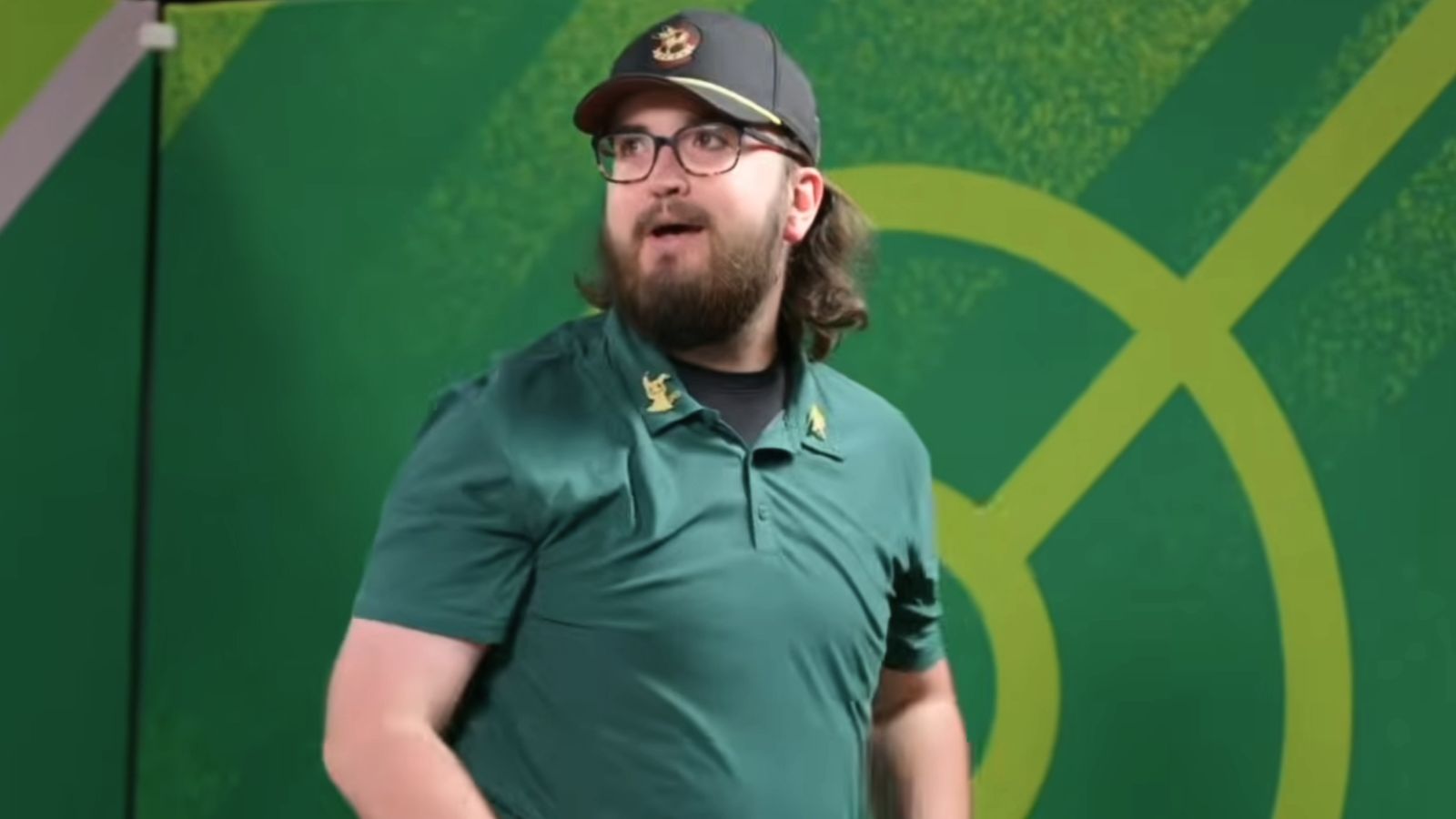 A Black man with a goatee wears a black t-shirt and is staring at the camera.